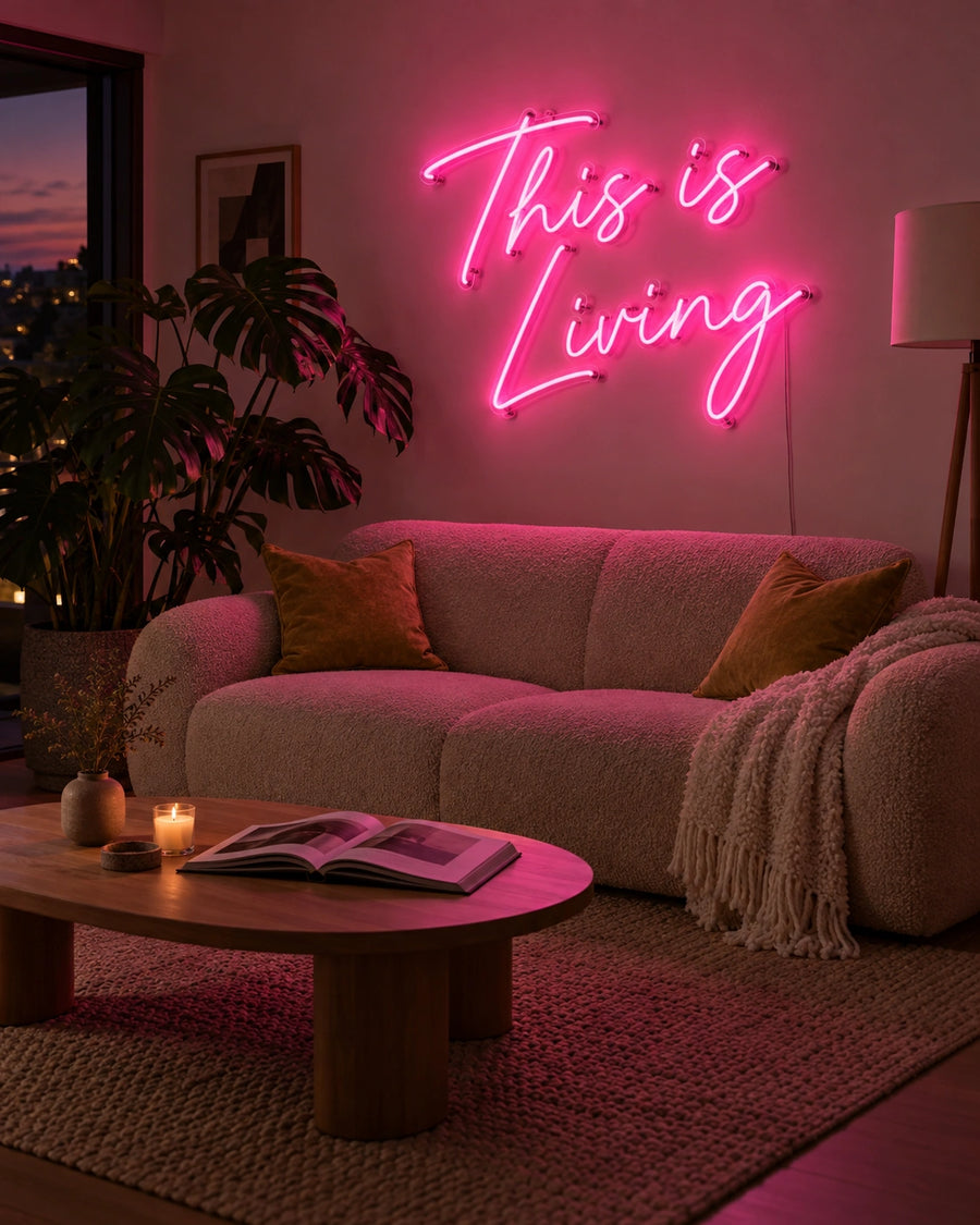 This Is Living pink LED neon sign on a living room wall above a sofa