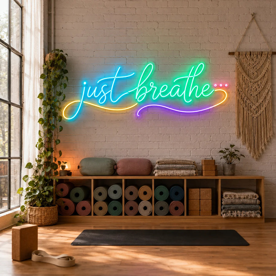 Just Breathe neon sign glowing on a yoga studio brick wall above rolled mats