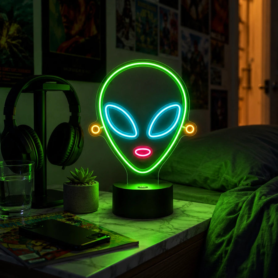 Alien head neon desk light glowing on a nightstand beside headphones and a plant