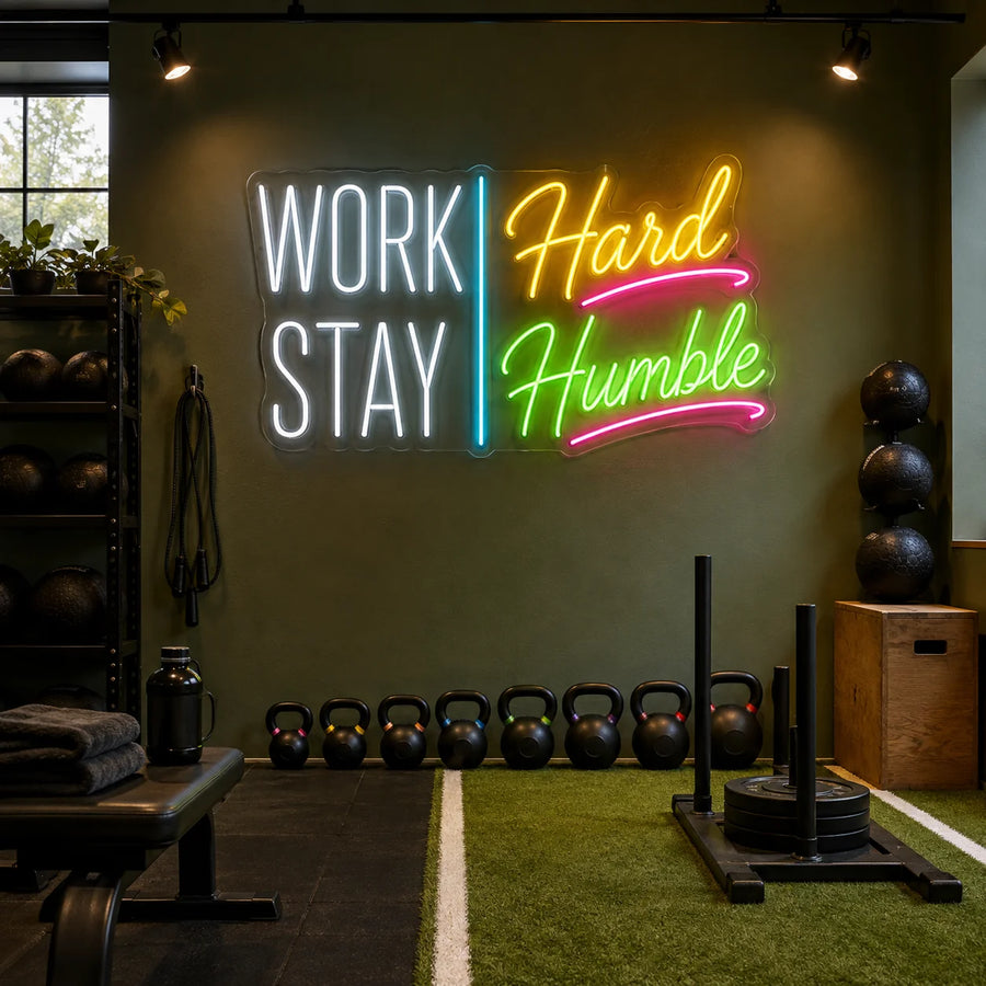 Work Hard Stay Humble neon sign glowing on a training studio wall above kettlebells and turf