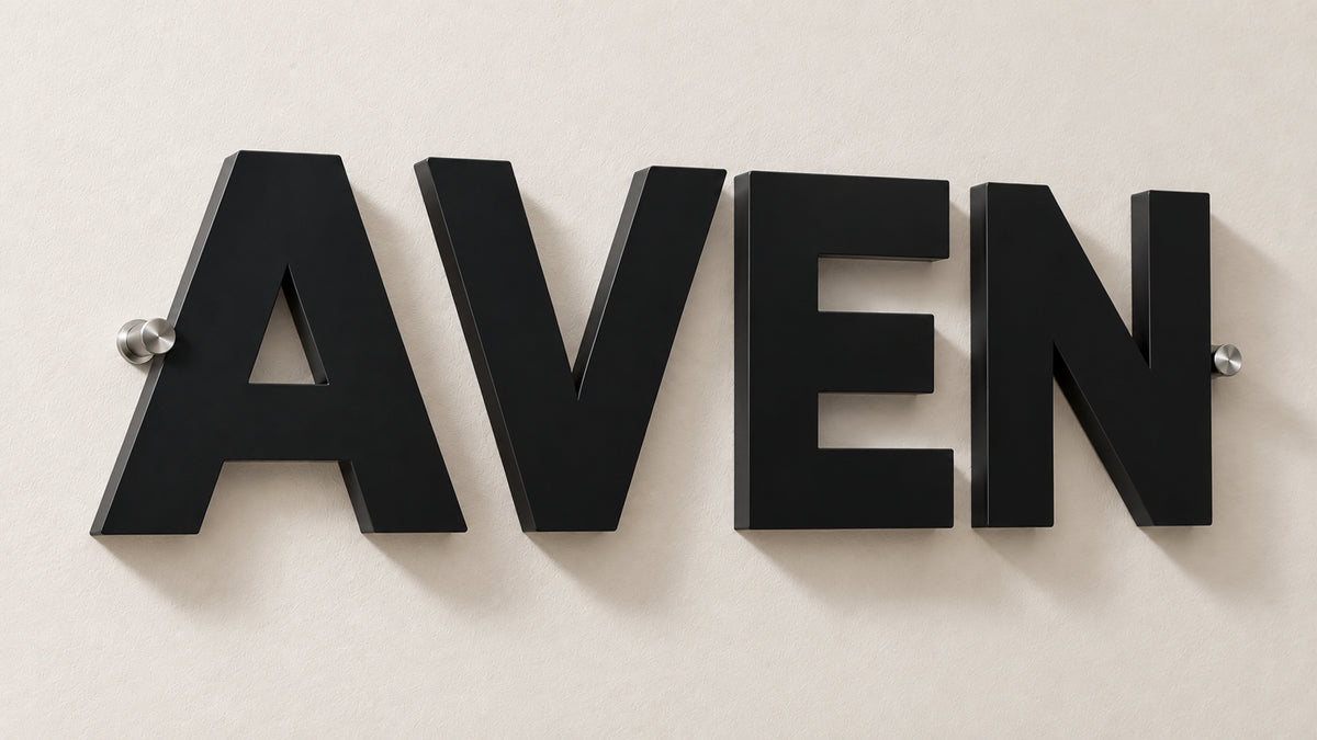 Non-illuminated dimensional matte black acrylic sign spelling AVEN on chrome standoffs casting a shadow on a pale wall