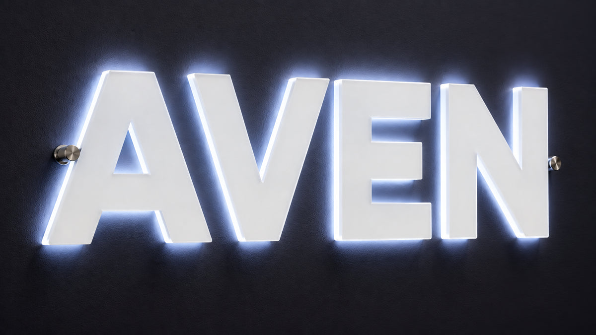 Backlit frosted acrylic lobby sign spelling AVEN on chrome standoffs with a cool white glow on a dark wall